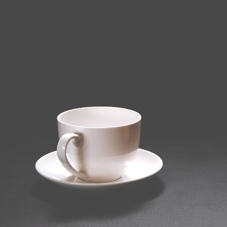 A white ceramic coffee cup stands on a black background. Close-up