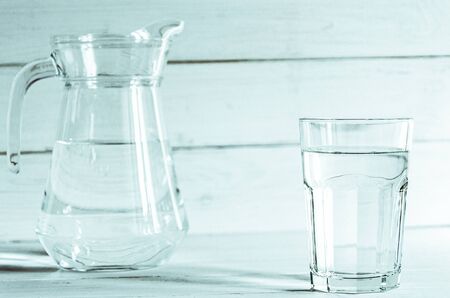 A glass of clean clear water stands on a white wooden background with sharp shadows. shadowsの写真素材