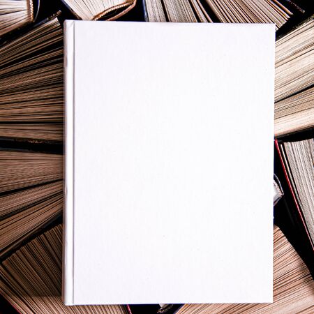 Mockup of closed blank square book at white textured paper background rests on open old multicolored...