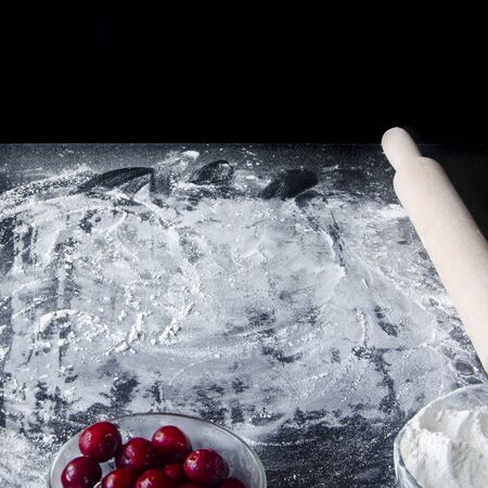 Flour and ingredients for sweet berry pie lie on the black table. Top view