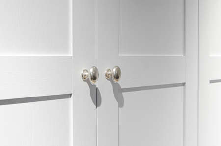 Furniture fittings. Metallic silver door handles with sharp shadows on the white wooden facadeの写真素材