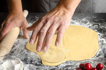 closeup of a young caucasian man kneading a piece of dough to prepare a coca de cireres, a cherry sweet flat cake typical of Catalonia, Spain, on a wooden tableの写真素材
