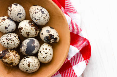 The quail eggs lie on a wooden plate on a white wooden tableの写真素材