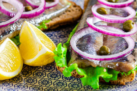 Appetizing sandwich with Norwegian herring, lettuce, blue onion, lemon and tomato lies on a wooden texture boardの写真素材