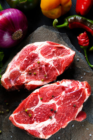 Meat raw steaks lie on a black background with vegetables, fresh blue onions, yellow peppers, chili. background image. side view, copy space, top viewの写真素材
