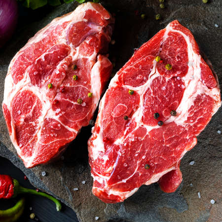 Meat raw steaks lie on a black background with vegetables, fresh blue onions, yellow peppers, chili. background image. side view, copy space, top viewの写真素材
