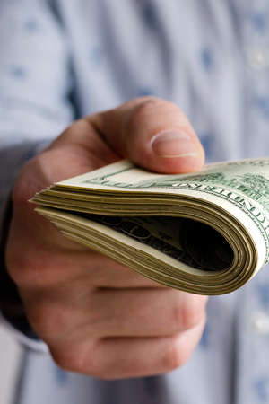 A bundle of American dollars money is rolled up in a hand.の写真素材