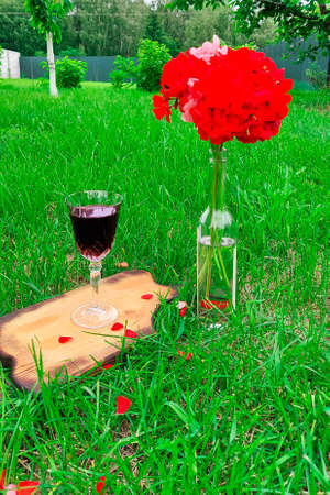 A glass of red wine stands on a wooden tray next to a bouquet of flowers in the gardenの写真素材