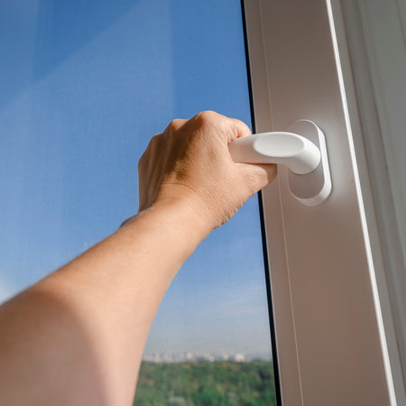 Woman's hand opens the handle of a plastic window against a blue skyの写真素材