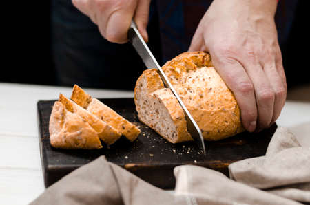 Whole grain bread put on kitchen wood plate with a chef holding gold knife for cut. Fresh bread on table close-up. Fresh bread on the kitchen table The healthy eating and traditional bakery conceptの写真素材