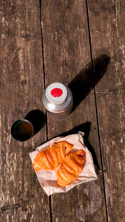 Picnic. A flask with tea and croissants are on a wooden table in the forestの写真素材