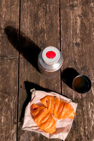 Picnic. A flask with tea and croissants are on a wooden table in the forestの写真素材