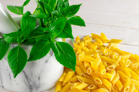 uncooked pasta on a wooden table isolated next to Fresh green basilの写真素材