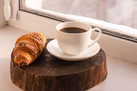A cozy concept. Classic winter breakfast. A cup of coffee and a croissant stand on the windowsill.の写真素材