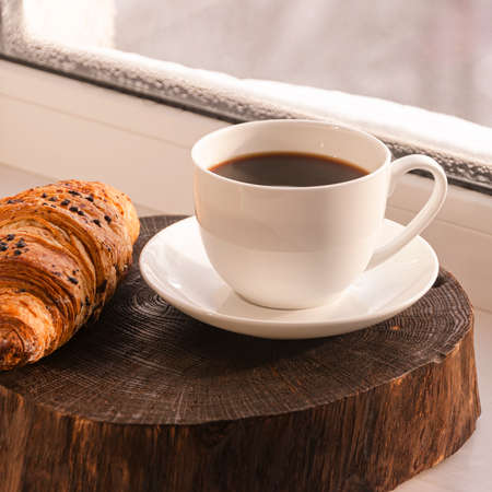 A cozy concept. Classic winter breakfast. A cup of coffee and a croissant stand on the windowsill.の写真素材