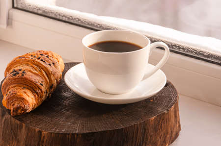 A cozy concept. Classic winter breakfast. A cup of coffee and a croissant stand on the windowsill.の写真素材