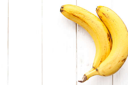 Ripe yellow bananas lie on a white wooden tableの写真素材