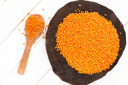 Red lentils and bulgur on a dark wooden plate and a wooden spoon standing on a white wooden table with copy space. Harvest conceptの写真素材