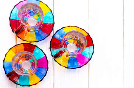 Multi-colored glass cups and saucers for coffee and tea stand on a wooden tray on the window sillの写真素材