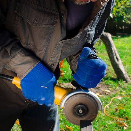Close-up on the sides fly bright sparks from the angle grinder machine. A young male welder in a...