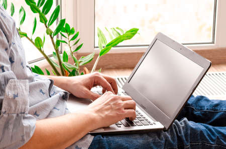 Close up low angle view of a man working from home on a laptop computer sitting at a desk surfing the internet. Remote working from home. Concept of distance learning, isolation, businessの写真素材