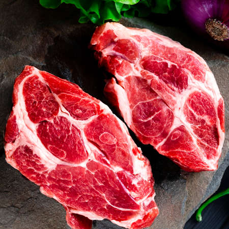 Meat raw steaks lie on a black background with vegetables, fresh blue onions, yellow peppers, chili. background image. side view, copy space, top viewの写真素材