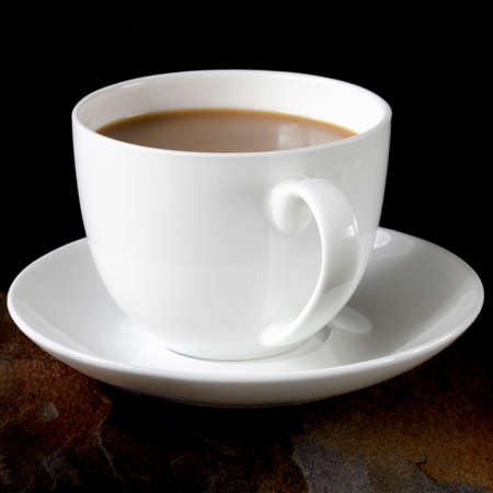 A white cup of coffee with a thick foam stands on a black table next to a multi-colored wild stone. Close-upの写真素材