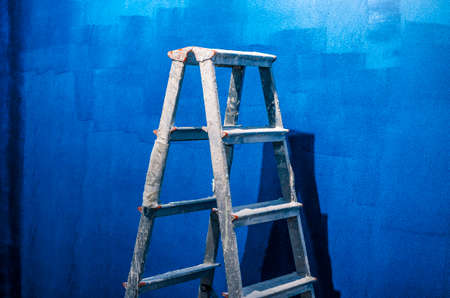 Close-up of metal ladder standing on blue wall. Equipment for worker to paint wall. Copy space in right side. Construction site and renovation conceptの写真素材