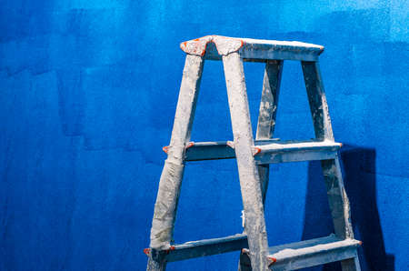 Close-up of metal ladder standing on blue wall. Equipment for worker to paint wall. Copy space in right side. Construction site and renovation conceptの写真素材