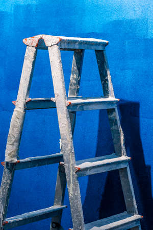 Close-up of metal ladder standing on blue wall. Equipment for worker to paint wall. Copy space in right side. Construction site and renovation conceptの写真素材