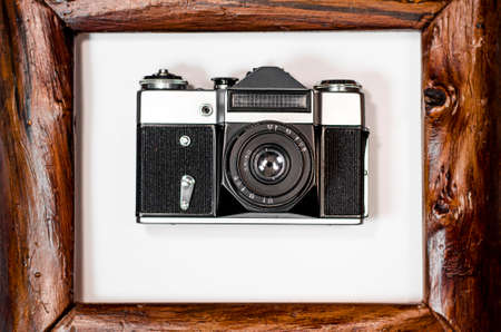 An old camera lies on a white background in a brown wooden frameの写真素材
