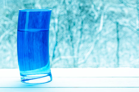 Deformed blue glass with clean spring water against the background of a snowy forestの写真素材