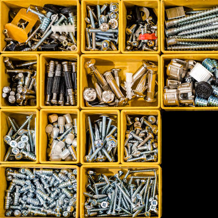 Yellow case with small construction objects. Many storage compartments filled with builders accessories containing screws, nuts, bolts, nails and other tools in workshop. Arranged neatly and organizedの写真素材