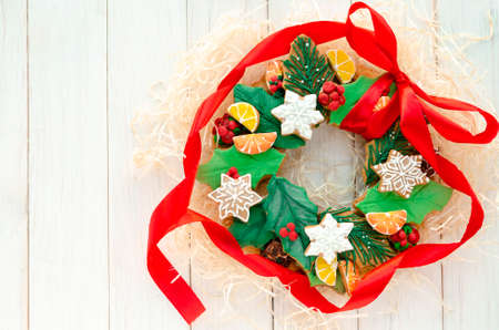 A Christmas gingerbread in the shape of a Christmas wreath lies on a white wooden background. Christmas card with space for text. Decorative composition of a Christmas wreath, gingerbread cookiesの写真素材