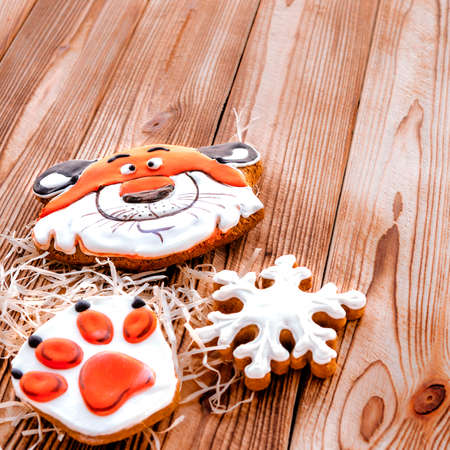 Christmas gingerbread in the shape of a tiger's head and paw lie on a wooden background. Christmas card with space for textの写真素材