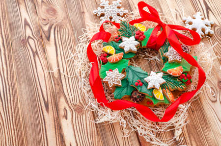 A Christmas gingerbread in the shape of a Christmas wreath lies on a wooden background. Christmas card with space for text. Decorative composition of a Christmas wreath, gingerbread cookiesの写真素材