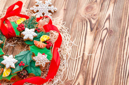 A Christmas gingerbread in the shape of a Christmas wreath lies on a wooden background. Christmas card with space for text. Decorative composition of a Christmas wreath, gingerbread cookiesの写真素材
