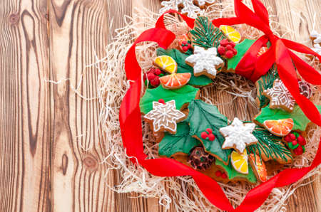 A Christmas gingerbread in the shape of a Christmas wreath lies on a wooden background. Christmas card with space for text. Decorative composition of a Christmas wreath, gingerbread cookiesの写真素材