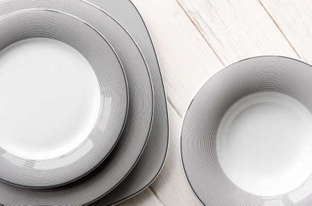 White round classical porcelain plates with a gray pattern stand on a white wooden tableの写真素材