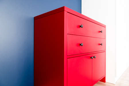 Interior design. Red wooden chest of drawers in Scandinavian style against a blue wallの写真素材