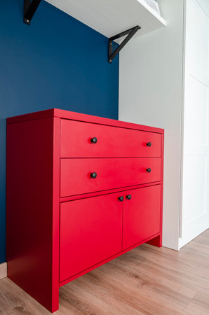 Red chest of drawers in a Scandinavian interior. A red wooden cabinet with black handles stands in an apartmentの写真素材