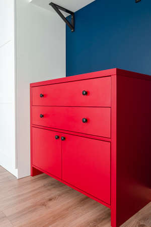 Red chest of drawers in a Scandinavian interior. A red wooden cabinet with black handles stands in an apartmentの写真素材