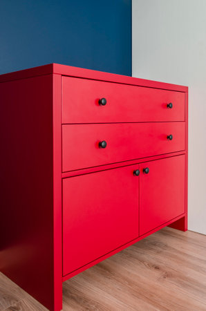 Red chest of drawers in a Scandinavian interior. A red wooden cabinet with black handles stands in an apartmentの写真素材
