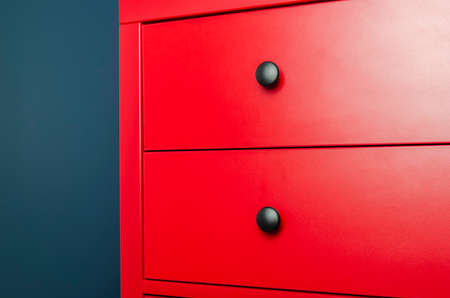 Red chest of drawers in a Scandinavian interior. A red wooden cabinet with black handles stands in an apartmentの写真素材