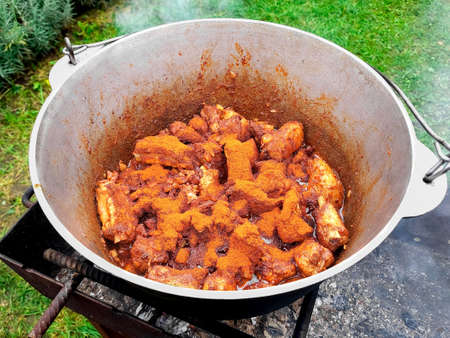 Delicious hungarian goulash in a kettle made outdoor at campfire. Beef meat marinated in adjika is stewed in a cauldron with tomatoes, bell peppers, parsley and cilantro, onions.の写真素材