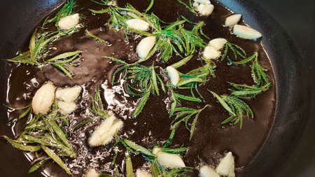 Black cast iron frying pan with ingredients for cooking: oil, fresh green rosemary, raw garlic cloves. flat lay top view with space for textの写真素材