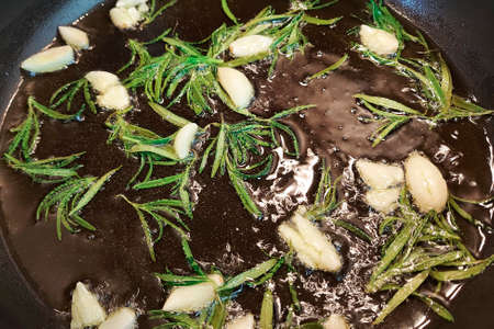Black cast iron frying pan with ingredients for cooking: oil, fresh green rosemary, raw garlic cloves. flat lay top view with space for textの写真素材