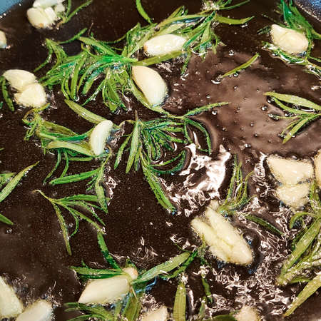 Black cast iron frying pan with ingredients for cooking: oil, fresh green rosemary, raw garlic cloves. flat lay top view with space for textの写真素材