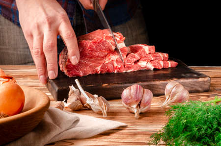 Butcher cutting pork meat on kitchen. The chef cuts the pork meat. On the background of vegetables. On a black background.Butcher shop.Recipes with meatの写真素材
