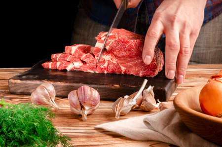 Butcher cutting pork meat on kitchen. The chef cuts the pork meat. On the background of vegetables. On a black background.Butcher shop.Recipes with meatの写真素材